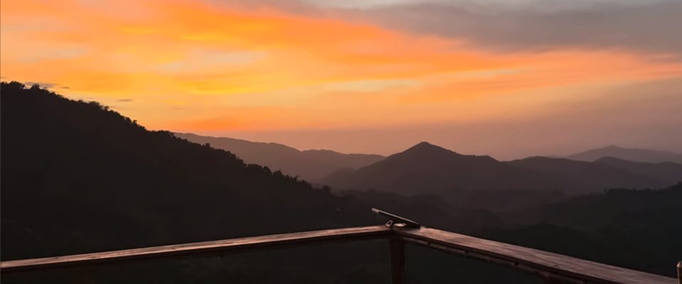 Atardecer naranja sobre las montañas de la Sierra Nevada de Santa Marta, visto desde una baranda de madera.