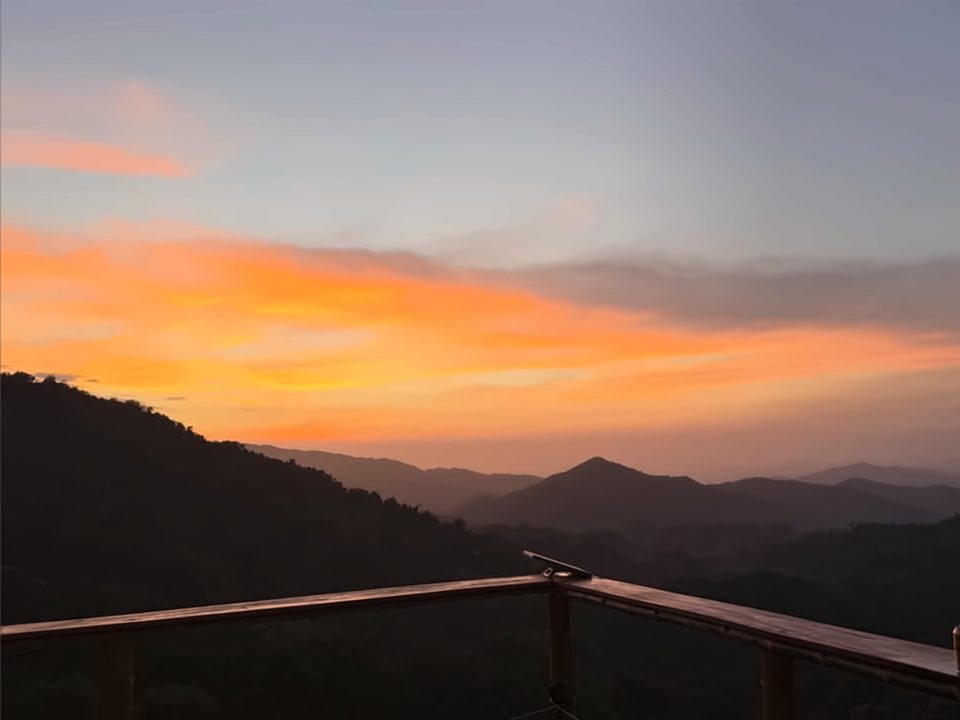 Atardecer naranja sobre las montañas de la Sierra Nevada de Santa Marta, visto desde una baranda de madera.