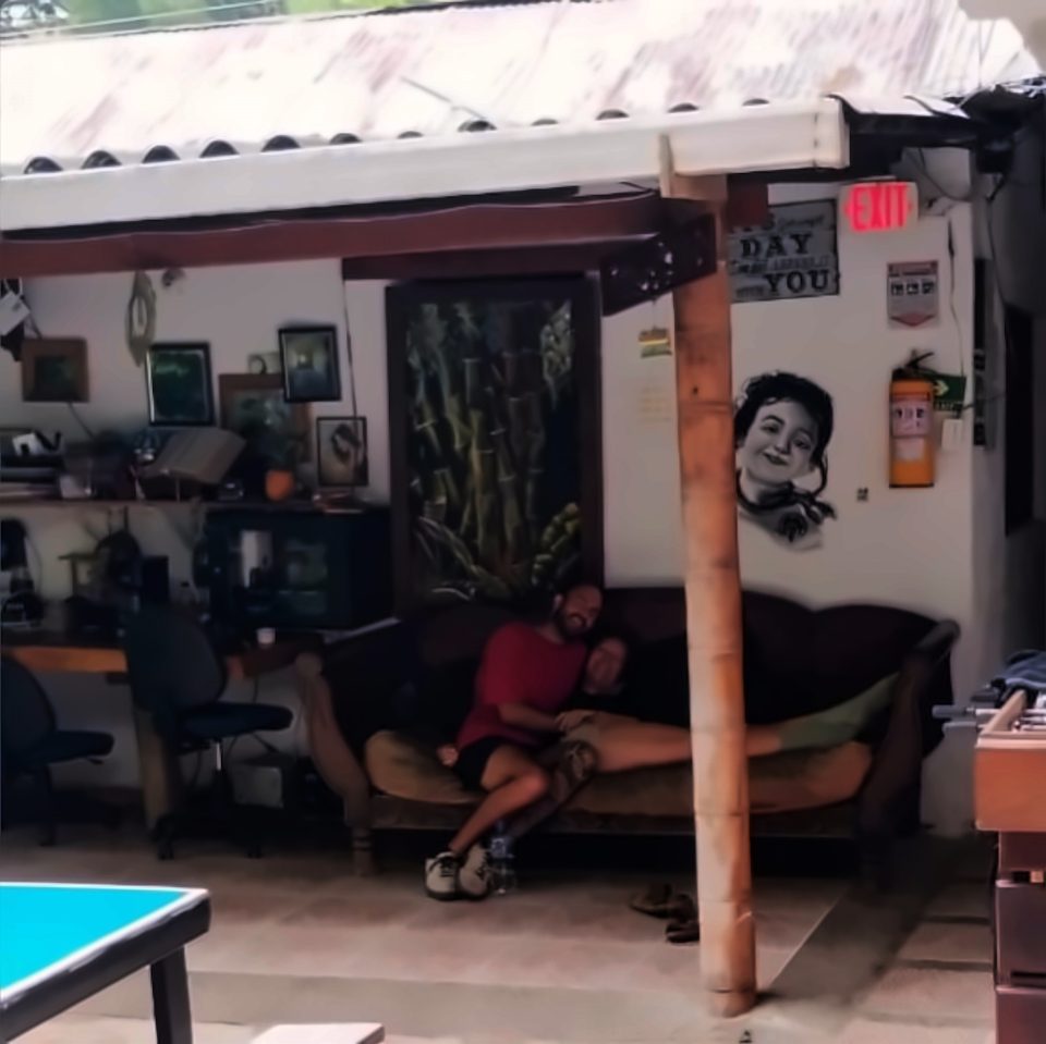 Dos personas descansan abrazadas en un sofá de la sala común cubierta; en primer plano una mesa de ping-pong y a la derecha un futbolín.